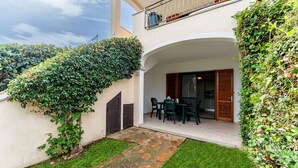 A covered outdoor seating area with a table and chairs, a stone pathway, and a view of a building with a balcony. - One bedroom apartment (4 people) - Le Dimore di Budoni (Budoni)