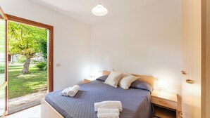 A bedroom with a bed, a nightstand, a lamp, and a view of a garden through a glass door. - One bedroom apartment (4 people) - Le Dimore di Budoni (Budoni)