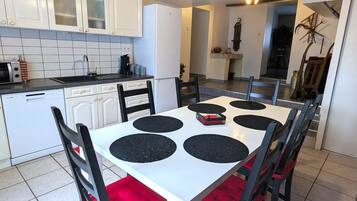 Cocina compacta con armarios blancos, lavavajillas y zona de comedor con mesa blanca y posavasos negros.