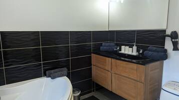 Une salle de bain moderne avec une baignoire blanche, des murs carrelés en noir et blanc, un meuble-lavabo en bois et un sèche-cheveux fixé au mur.