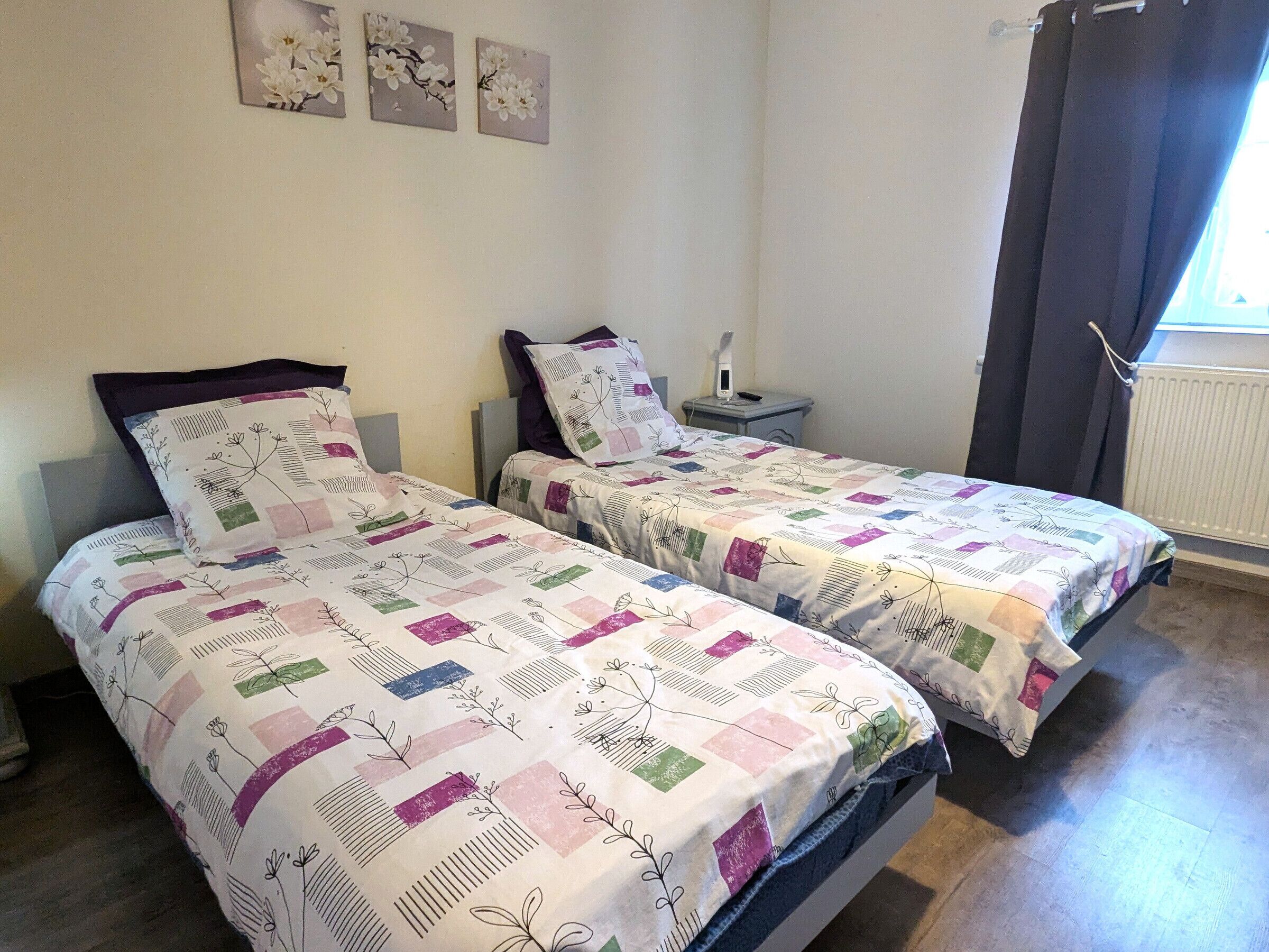 Un dormitorio con dos camas, una mesita de noche, una lámpara y un ventanal con cortinas.