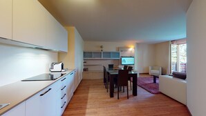 A modern kitchen with white cabinets, a built-in oven, and a dining area with a table and chairs.