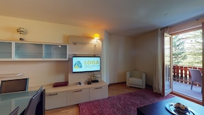 A modern living room with a flat-screen TV displaying 'LOGA', a sofa, a small table, and a balcony with a view.