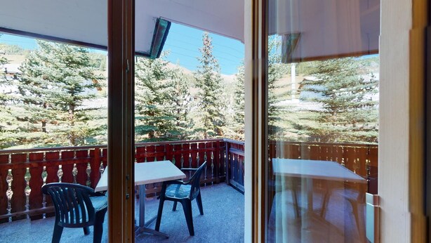 A balcony with a table and chairs, overlooking a forested area with tall trees.
