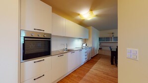 A modern kitchen with white cabinets, a built-in oven, a sink, and a wooden floor.