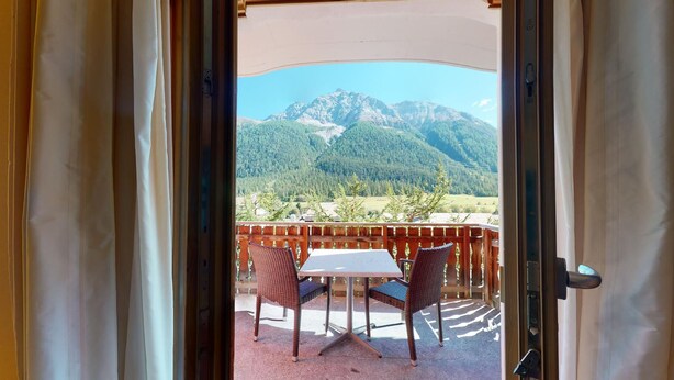 A balcony with a table and two wicker chairs, overlooking a mountainous landscape. - Modern 3½ room flat on the ground floor, approx. (Madulain)