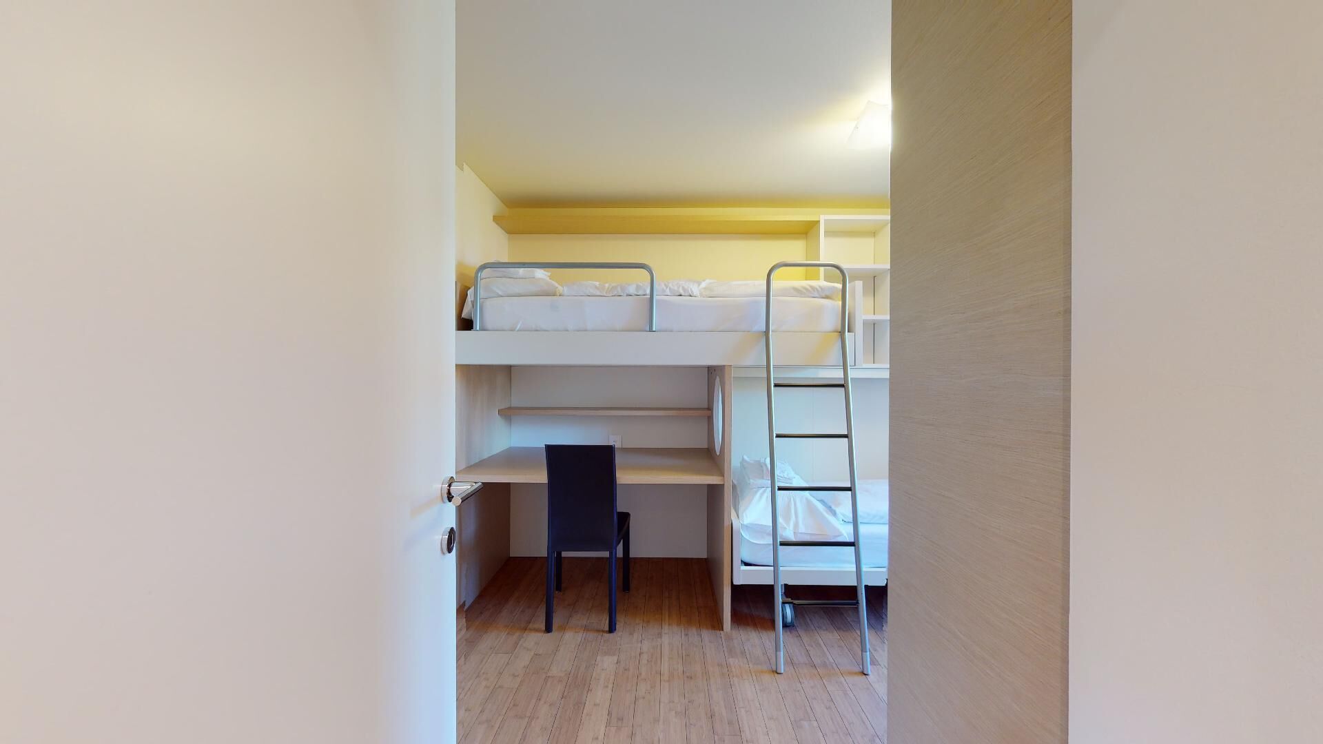 A bunk bed room with a desk and chair, a ladder, and a door.