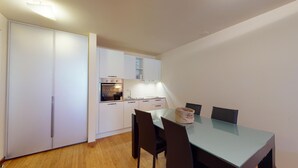 A compact kitchen with white cabinets, a built-in oven, and a dining area with a glass table and chairs. - Modern 3½ room flat on the ground floor, approx. (Madulain)