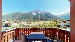 A balcony with a table and chairs, overlooking a mountainous landscape with a clear sky.