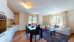 A modern living room with a dining area, a sofa, and a kitchen with a stove and cabinets. - Modern 3½ room flat on the ground floor, approx. (Madulain)
