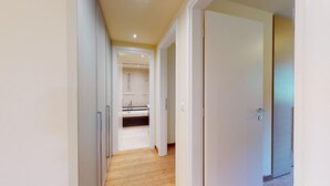 A narrow hallway leading to a kitchen with a wooden floor and white walls. - Modern 3½ room flat on the ground floor, approx. (Madulain)