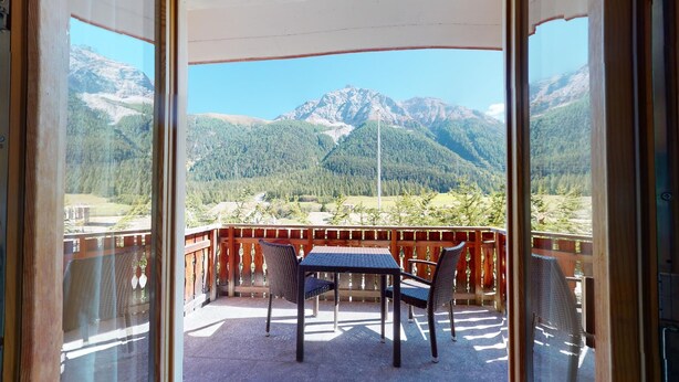 A balcony with a table and chairs, offering a view of a mountainous landscape. - Modern 3½ room flat on the ground floor, approx. (Madulain)