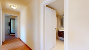 A hallway leading to a bathroom with a white door, a mirror, and a sink. - Modern 3½ room flat on the ground floor, approx. (Madulain)