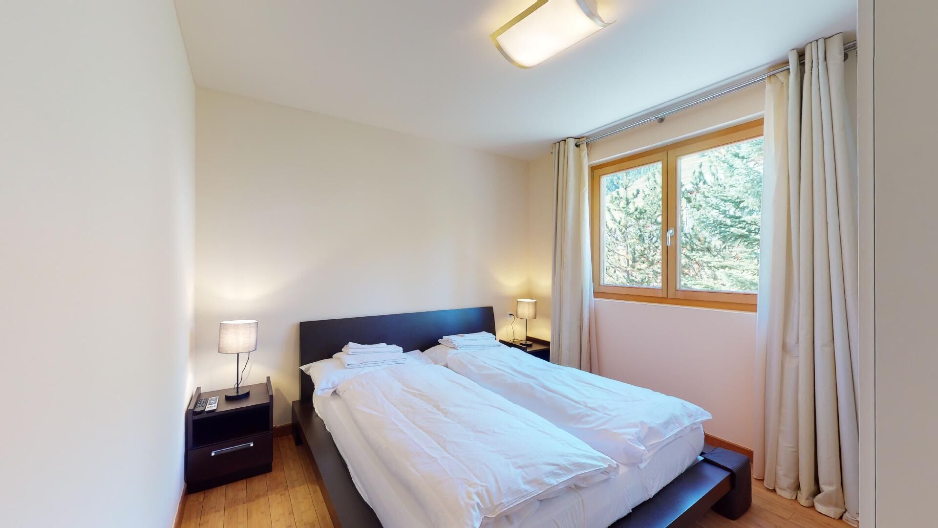Une chambre à coucher avec un lit, des lampes de chevet, une table de chevet et une fenêtre avec des rideaux.