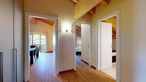 A corridor with wooden floors and white walls, leading to a balcony with a table and chairs. - Modern 3½ room flat on the ground floor, approx. (Madulain)