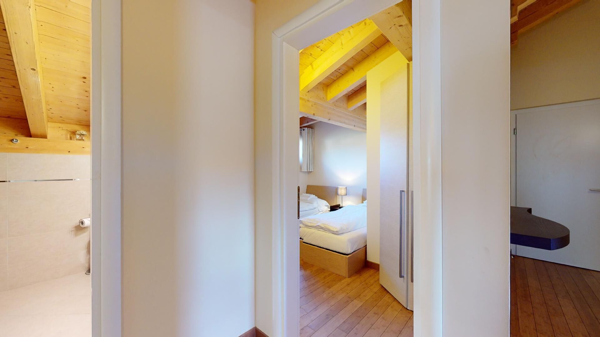 Ein Hotelzimmer mit Holzboden, einem Bett mit weißer Bettwäsche, einem Nachttisch und einem Beistelltisch.