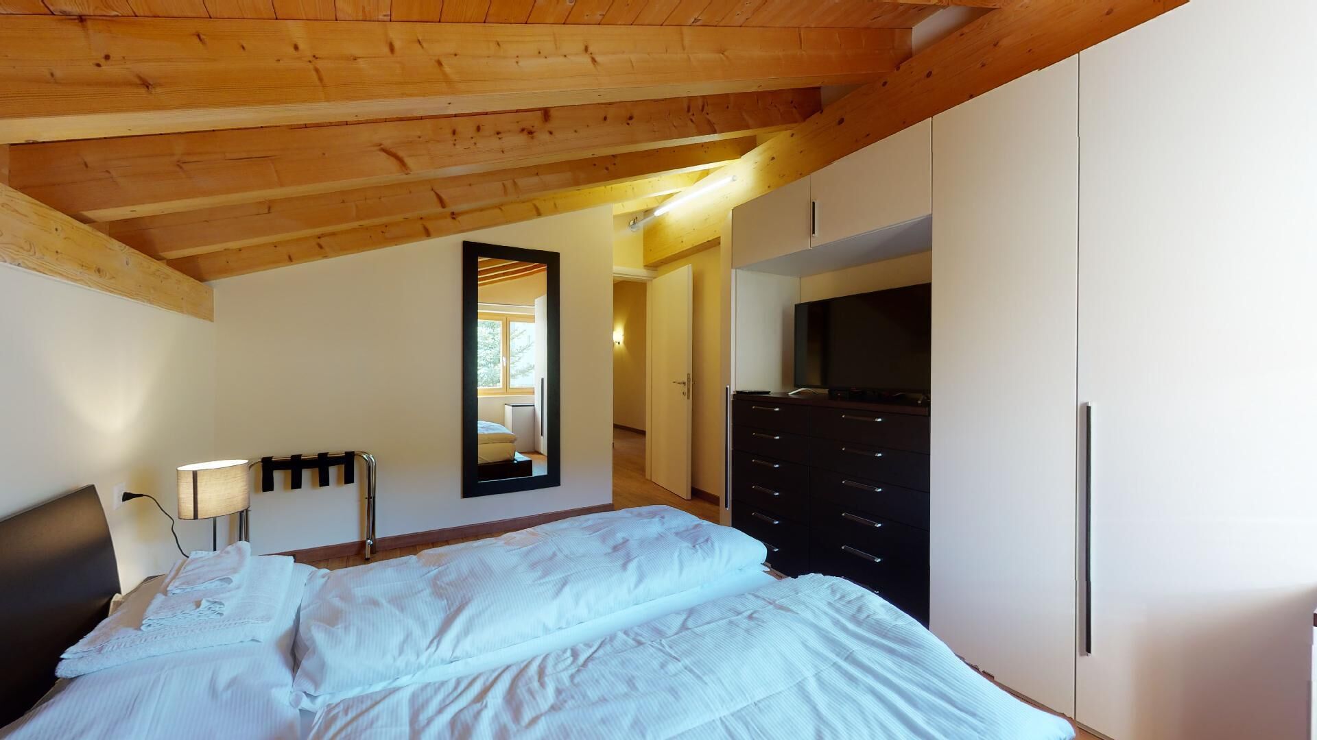 Un dormitorio con techo de madera, una cama, un aparador, un televisor y un espejo.