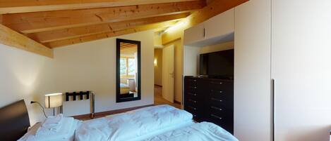 Un dormitorio con techo de madera, una cama, un aparador, un televisor y un espejo.