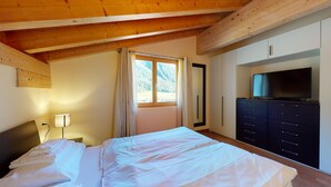 Quarto com cama, televisão em penteadeira e janela com cortinas.