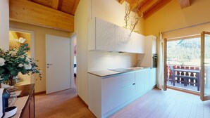 Uma cozinha moderna com armários brancos, forno embutido e uma janela grande com vista para um deck de madeira.