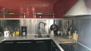 A modern kitchen with stainless steel appliances, a red tiled backsplash, and black cabinets. - Spacious Gîte with Private Pool, Near Nature Park & Attractions in Lorraine (Athienville)