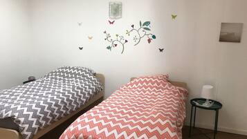 A room with two beds, each with patterned bedding, a small table with a lamp, and a wall decal with butterflies and flowers.