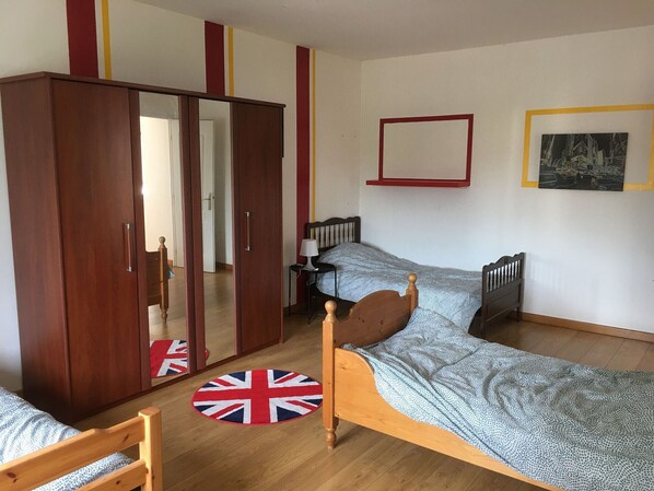 Un dormitorio con un armario de madera, una cama individual con una manta estampada, una alfombra redonda con diseño de la bandera del Reino Unido y un cuadro en la pared.