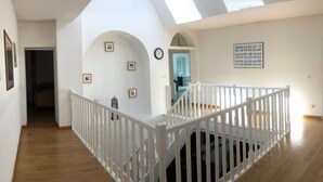 A spacious interior with a wooden floor, white walls, and a white railing. There are framed pictures on the walls and a clock. - Spacious Gîte with Private Pool, Near Nature Park & Attractions in Lorraine (Athienville)