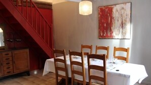 A dining area with a table set for four, wooden chairs, a red staircase, and a modern abstract painting on the wall.