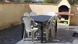 Eine Terrasss mit Tisch, Stühlen, einem Pizzaofen und einem gefliesten Boden.