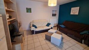 Ein Wohnzimmer mit einem weißen Sofa, einem braunen Sofa, einem weißen Couchtisch, einem Fernseher und einem Gemälde an der Wand.