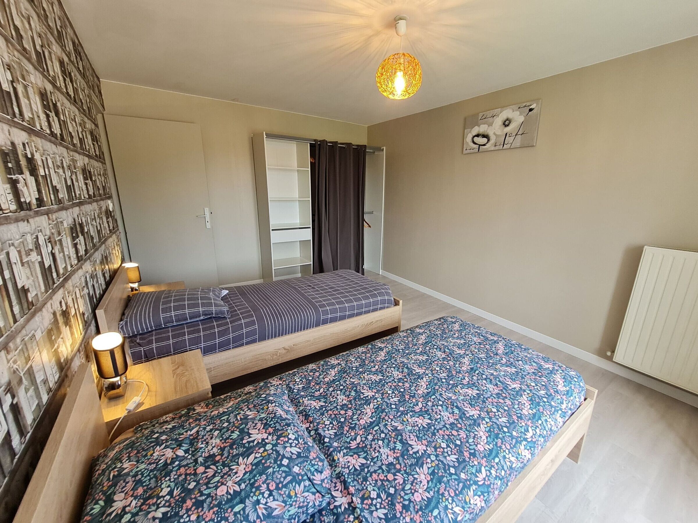 Een slaapkamer met twee bedden, een wandplank, een radiator en een plafondlamp.