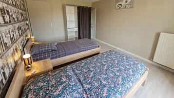 Een slaapkamer met twee bedden, een wandplank, een radiator en een plafondlamp.