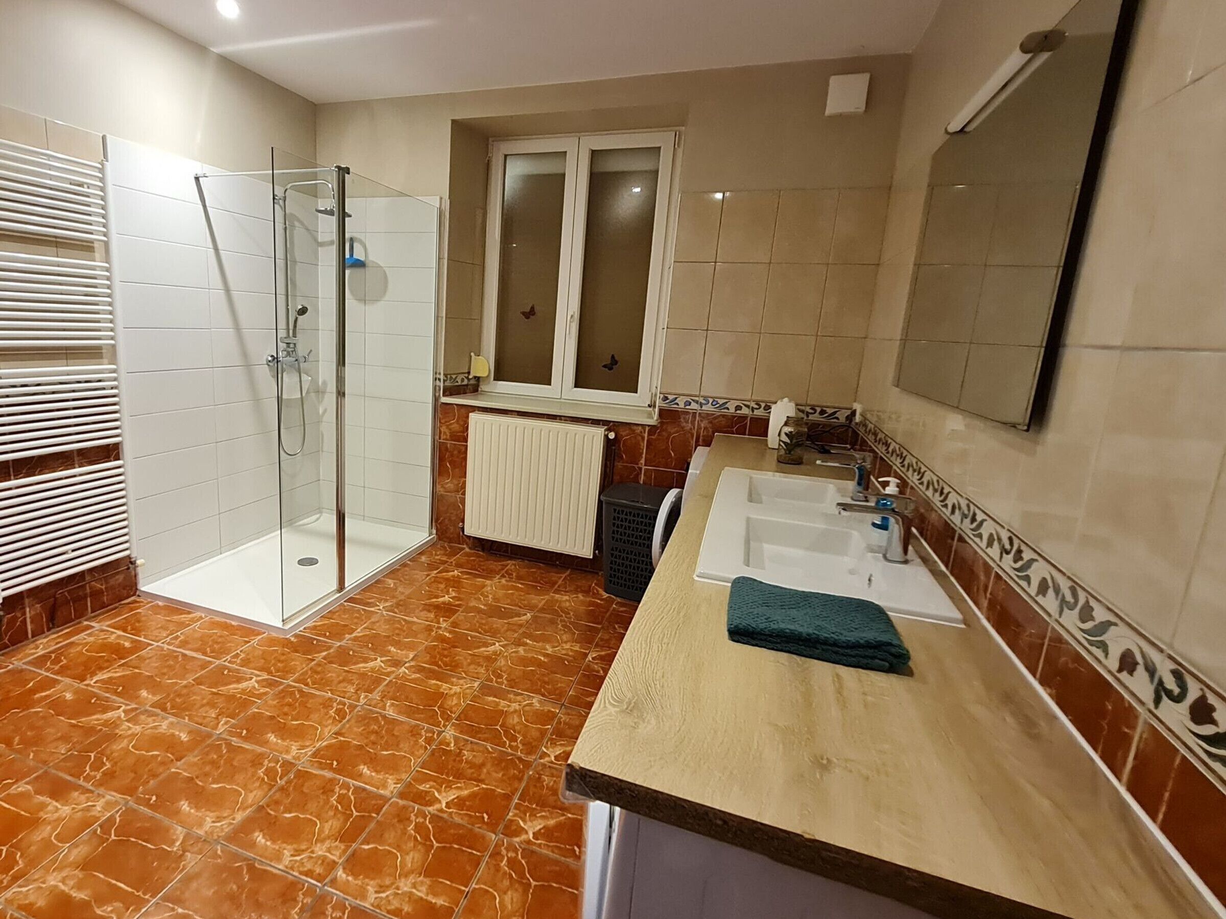 A bathroom with a glass shower enclosure, a sink with a towel, and a window above the mirror.