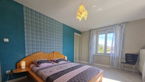 Ein Schlafzimmer mit einem Bett, einer Nachttischlampe, einem Fenster mit Vorhängen und einer Pendelleuchte.