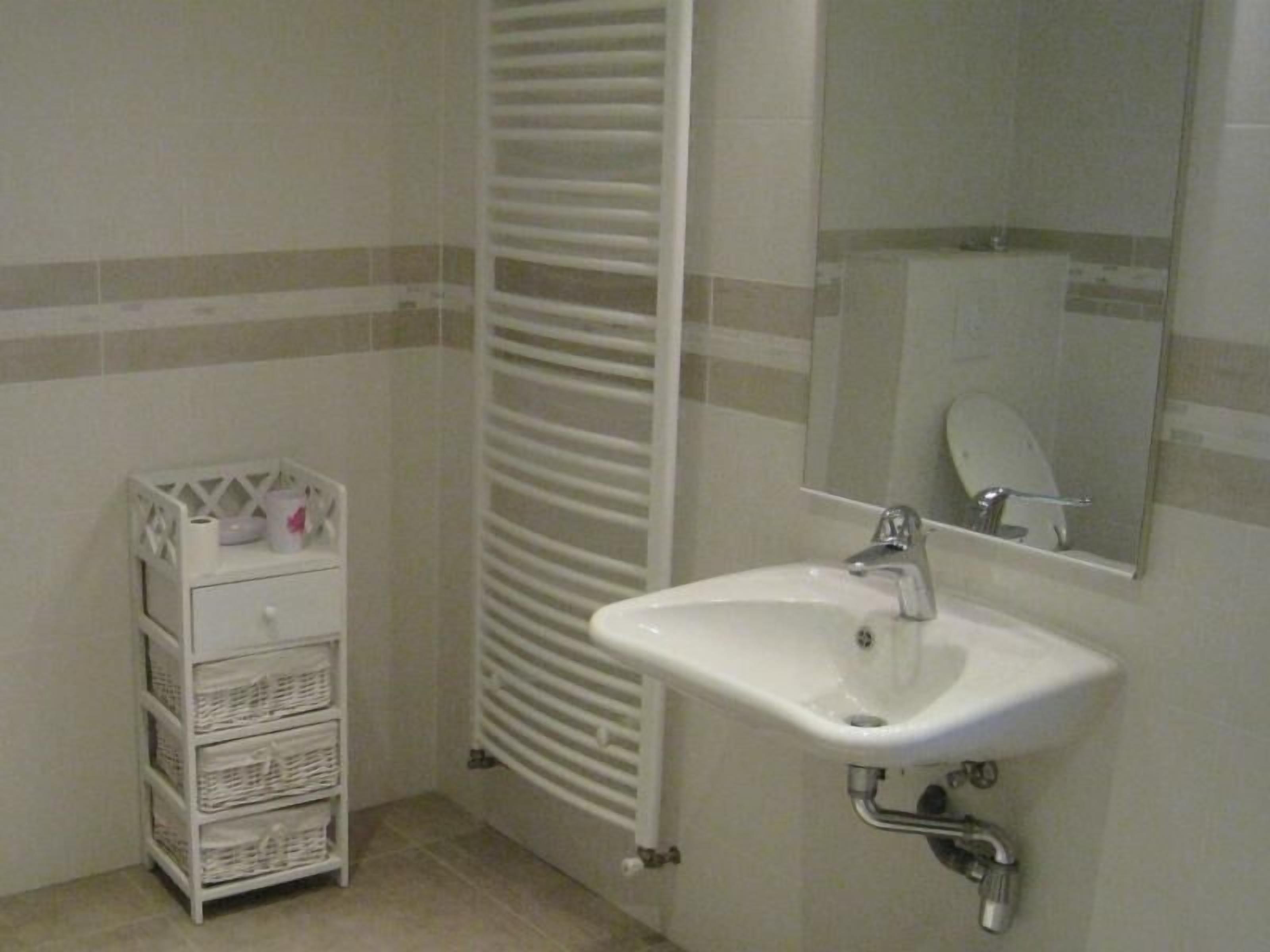 Une salle de bain avec un lavabo blanc, un miroir et un porte-serviettes blanc sur lequel sont pliés des serviettes.