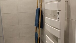 Ein Badezimmer mit Fliesenboden, einer an der Wand lehnten Holzleiter und einem weißen Schrank mit Bedienfeld.