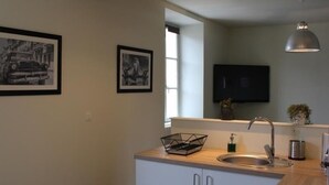 Eine moderne Küche mit Holztischplatte, Spüle aus Edelstahl und zwei Schränken. An der Wand hängen zwei Bilder und über der Spüle befindet sich ein Fernseher.