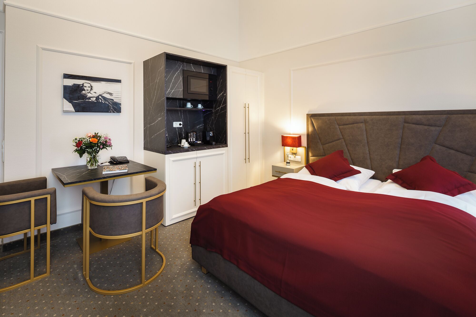 Habitación de hotel con cama, escritorio, silla, mesita de noche y televisor montado en la pared.