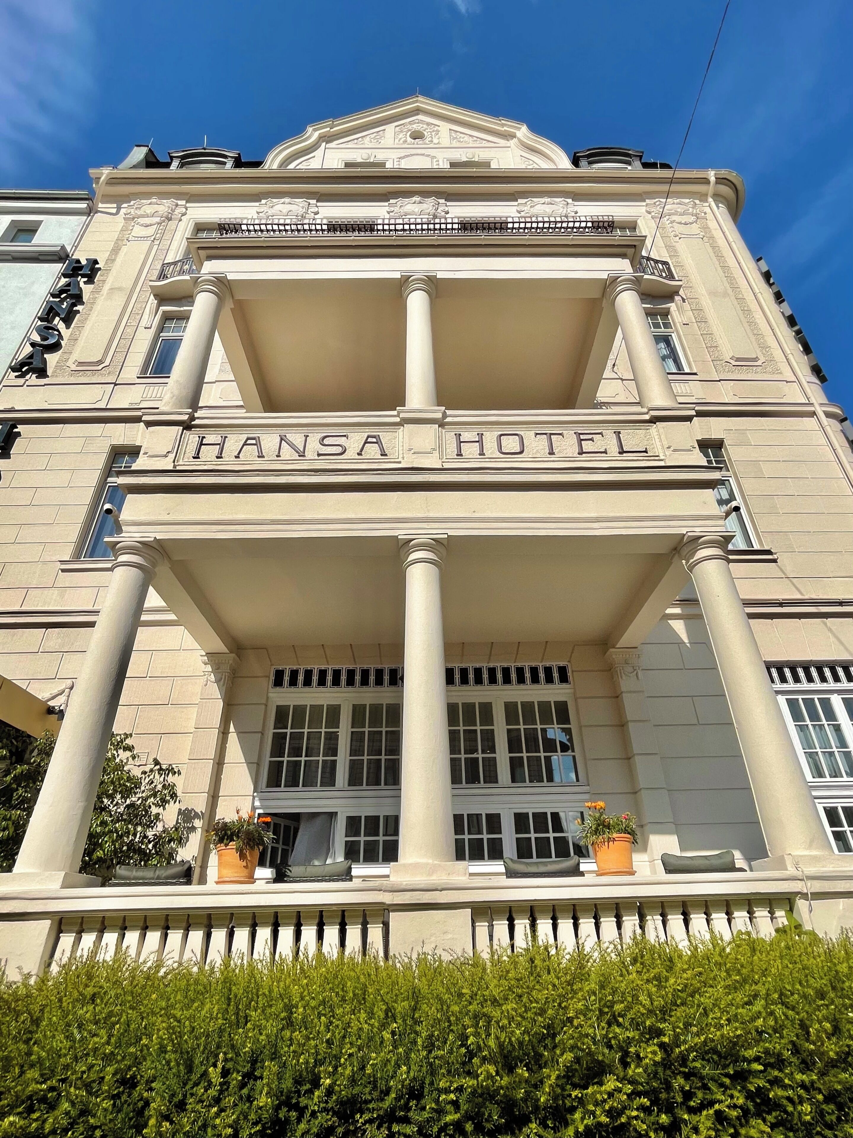 Un edificio con un letrero que dice 'Hansa Hotel' sobre la entrada, con un estilo arquitectónico clásico que incluye columnas y un balcón.
