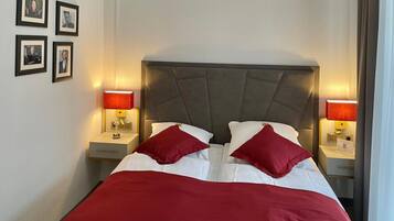 A neatly made double bed with red pillows, two bedside lamps, and framed pictures on the wall.