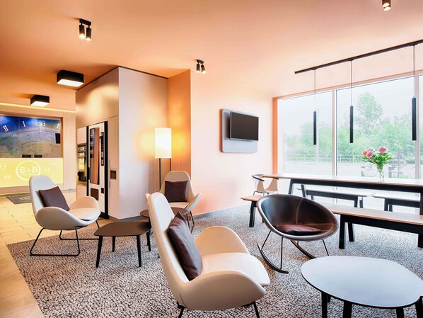 A modern hotel lobby with seating, a reception desk, and a large window offering a view of the outdoors. - B&B Hotel Rostock-Hafen (Rostock)