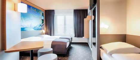 A hotel room with a bed, a desk, a chair, a small ottoman, a TV, and a window with curtains.