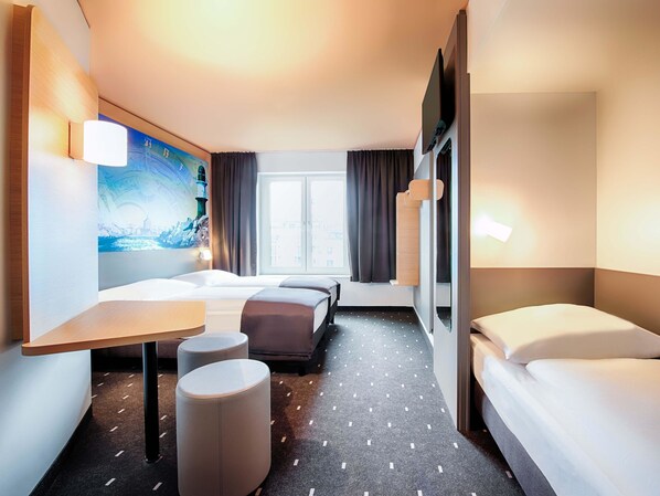 A hotel room with a bed, a desk, a chair, a small ottoman, a TV, and a window with curtains. - B&B Hotel Rostock-Hafen (Rostock)