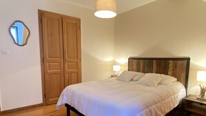 Een slaapkamer met een houten bed, twee nachtkastjes met lampen, een houten garderobe en een spiegel aan de muur.