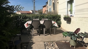 A patio with a table and chairs, surrounded by a hedge and a building with a window. - Charming 19th Century House in Mirabelle Country with Terrace and BBQ (Rozelieures)