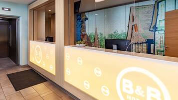 A reception area with a B&B Hotels sign, a reception desk, a potted plant, and a view of the outside.
