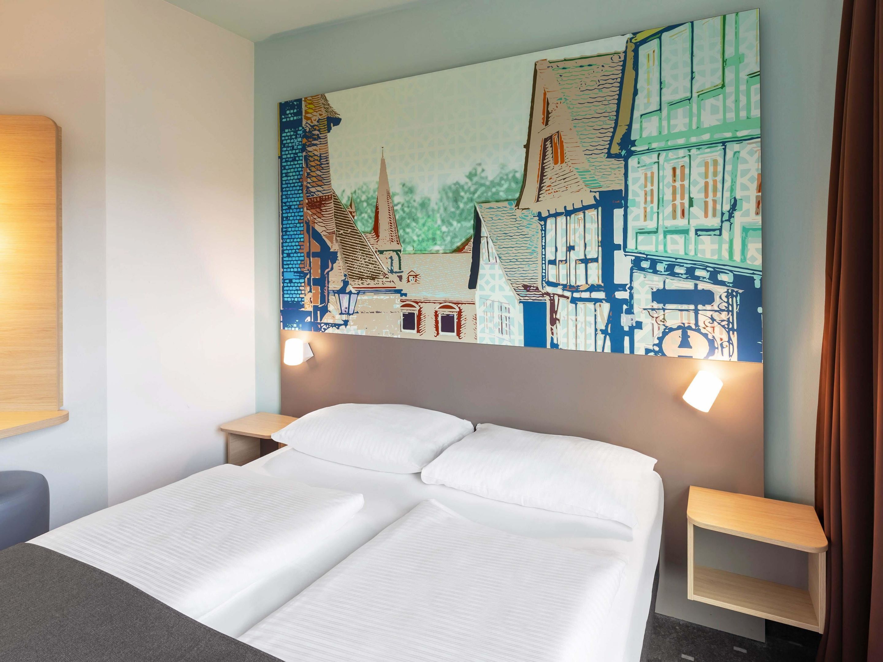 Een hotelkamer met een bed, twee nachtkastjes en een groot muurdecoratie met een stadsgezicht.
