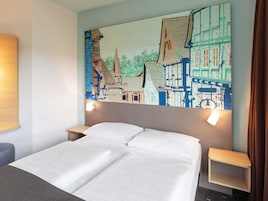 A hotel room with a bed, two bedside tables, and a large wall mural depicting a cityscape.