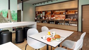 A modern breakfast area with a white table, black stools, and a counter displaying breakfast items.
